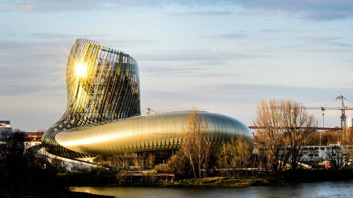 exterior of a curved golden building alongside a river