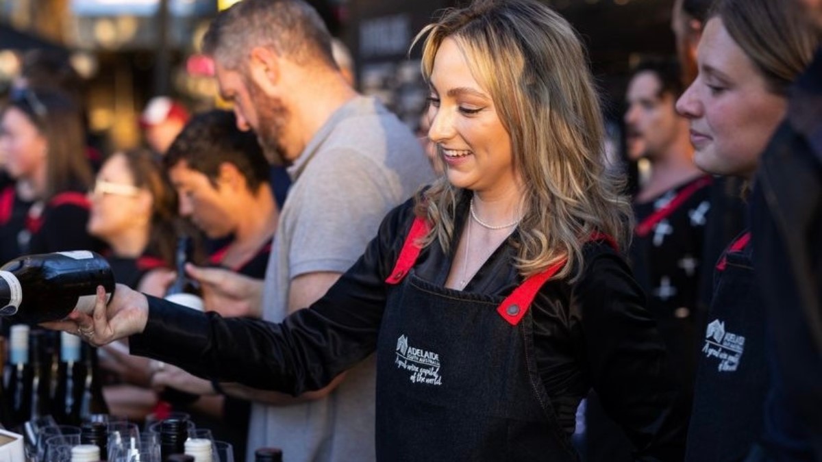 smiling woman behind a bar with other staff pouring wine