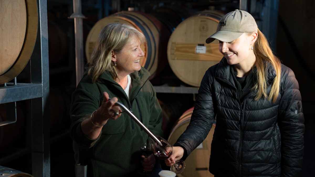 mother and daughter sampling wine in front of wine barrels