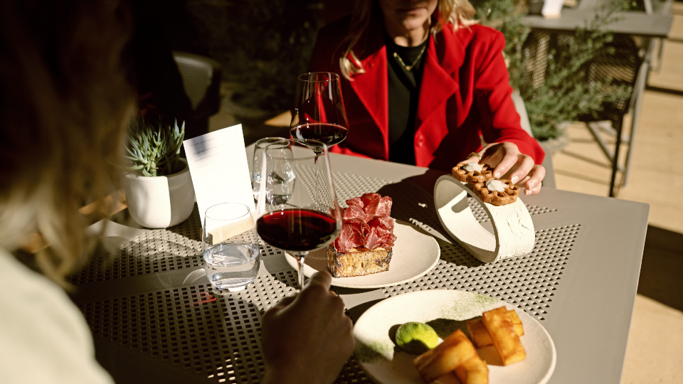 Two people enjoy wine and food at an outdoor table.