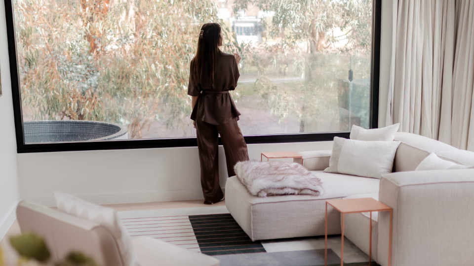 A woman in a room with comfortable modern furnishings looking out a window.