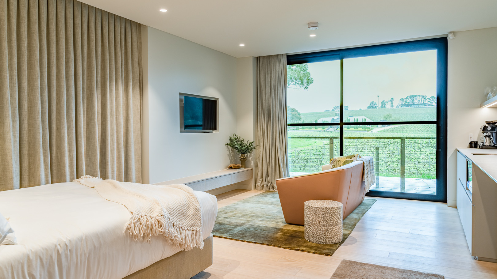 A pleasant room with a bed and furniture with a view looking out over a vineyard.